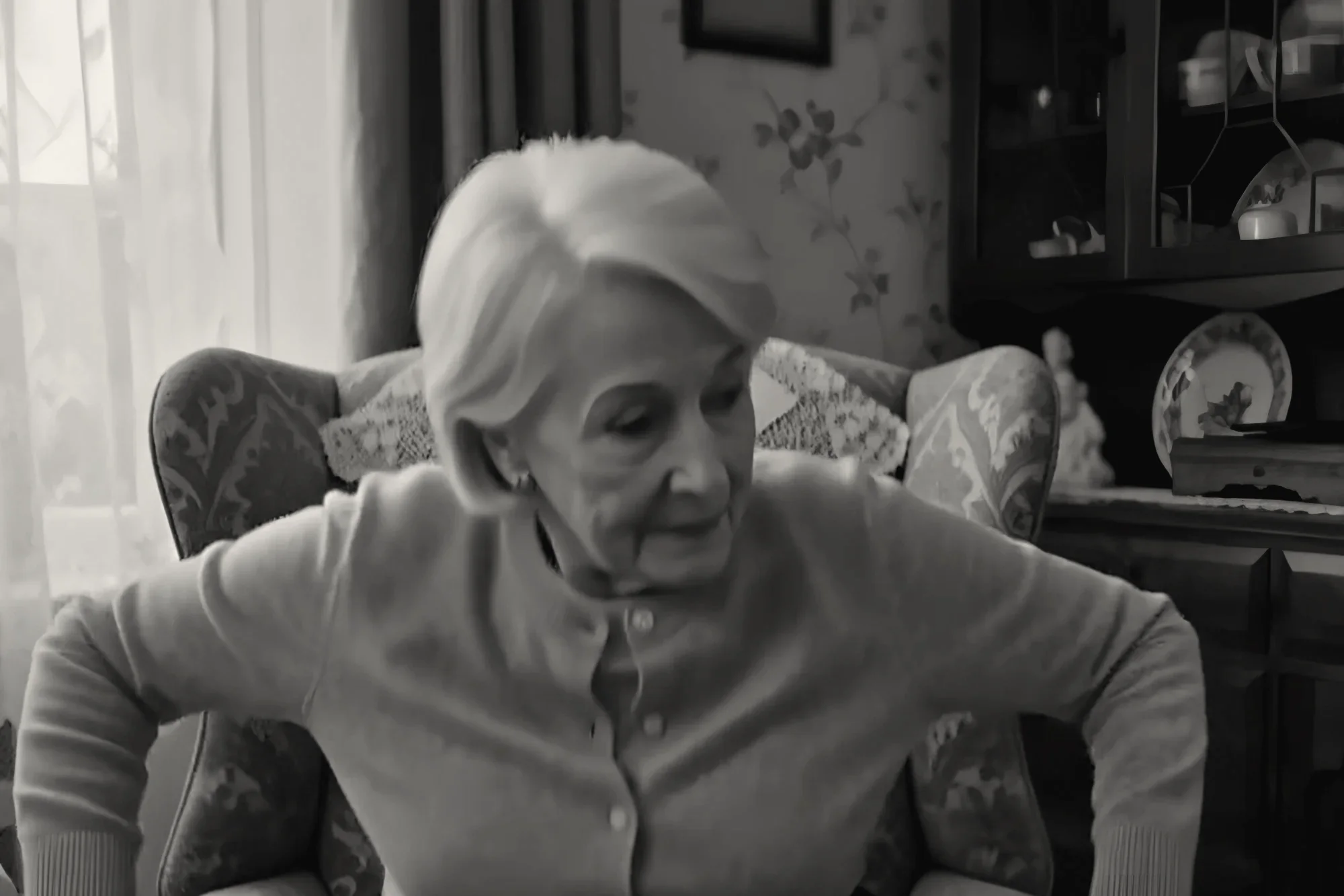 An older woman leaning forward and pushing on the armrests to rise from her armchair