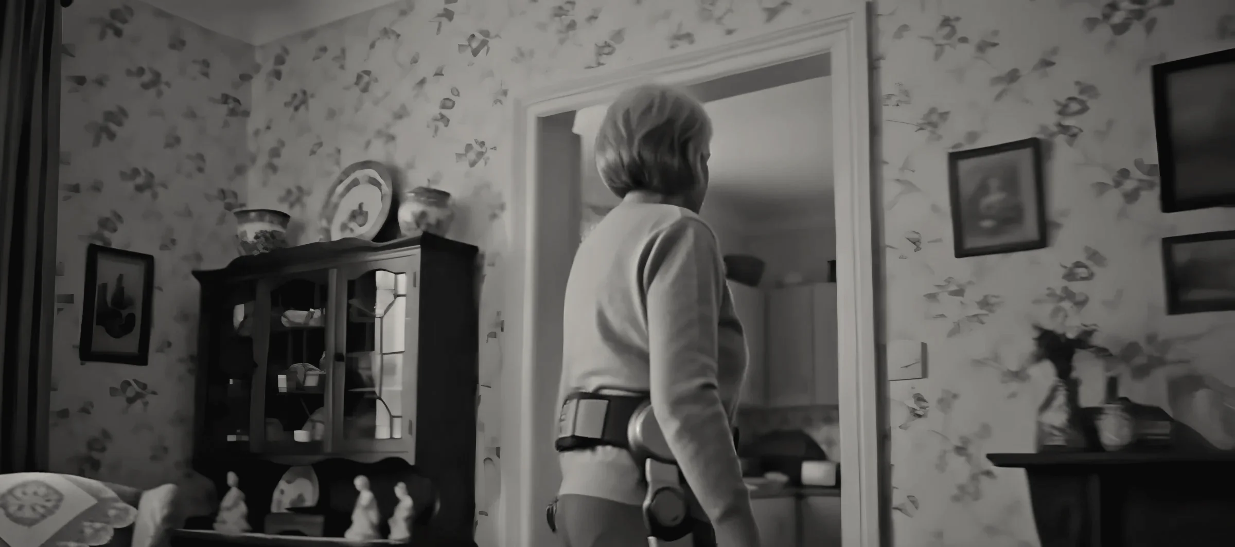 The woman seen from behind, walking toward the kitchen doorway